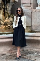 a lady in a long black dress with a belt and a white crop jacket